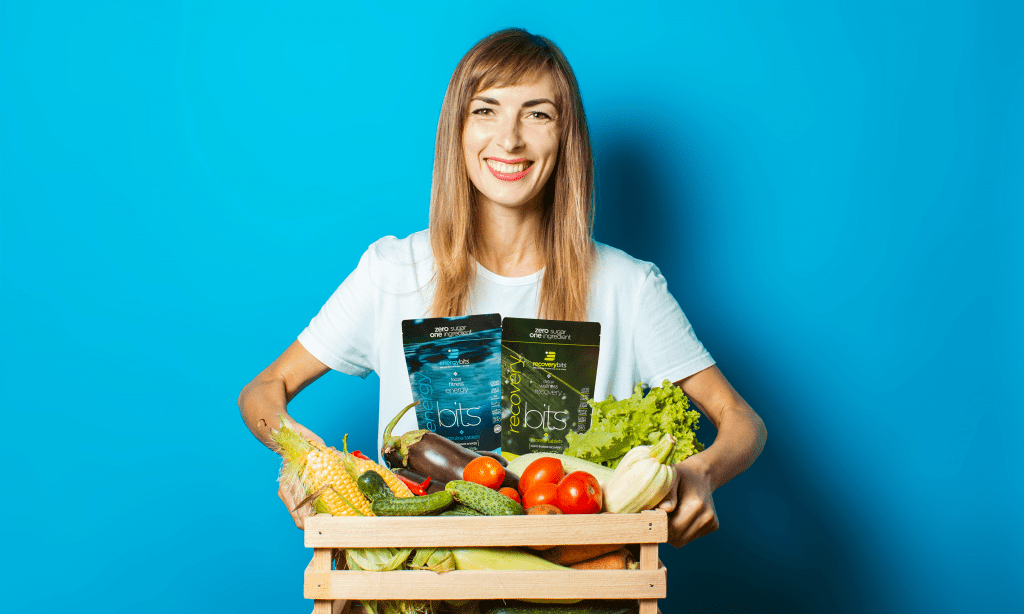 Woman carrying a box of fresh produce and a bag of RECOVERYbits and ENERGYbits 