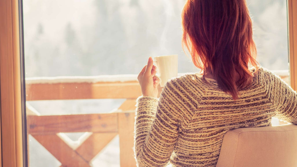 Woman drinking coffee while relaxing inside and looking at the snow
