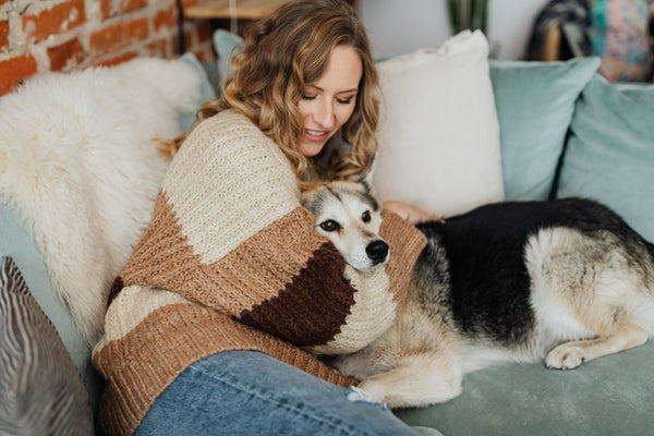 A woman wearing a knitted sweater lying with a white dog on the couch.
