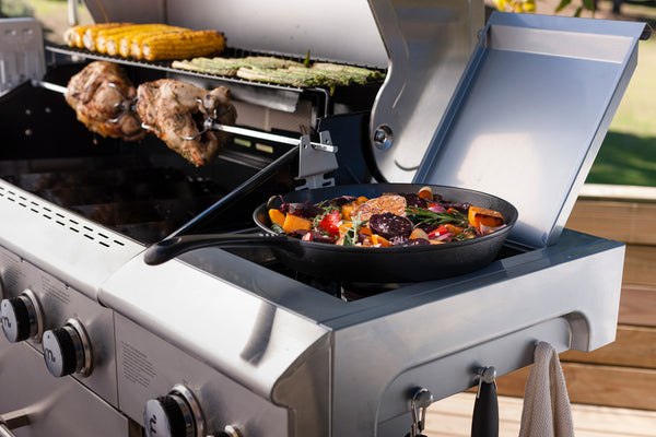 gas grill with meat on main grill and a sauce or side dish on side burner
