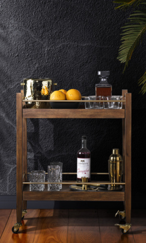 A wooden bar cart stands on wood floors in front of a black wall