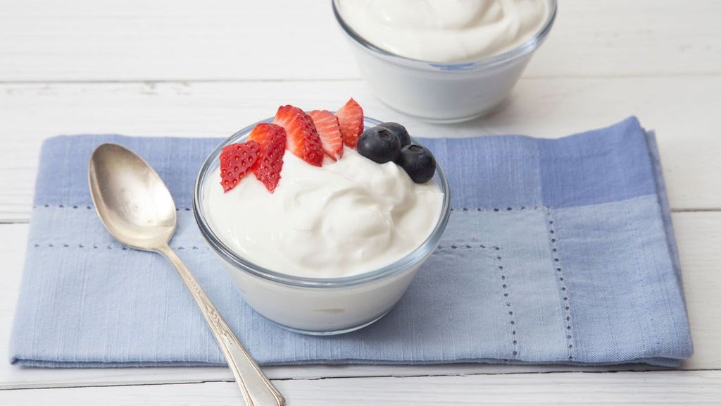 A bowl full of greek yogurt on a blue towel, with a spoon on the side. 