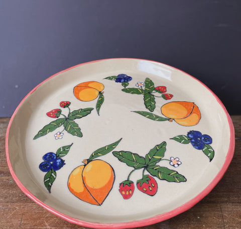ceramic plate with hand painted peach, blue berries and strawberries, with a pink border