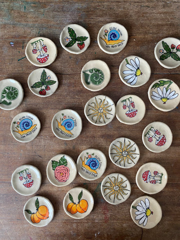 ceramic trinket dishes with various hand painted designs: sun, snail, strawberries, daisies, peonies, mushrooms, ferns