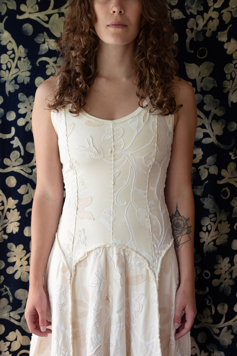 The Tenby Dress with hand-sewn seams, floral appliqué, and embroidery. Model is shown in Natural colorway.