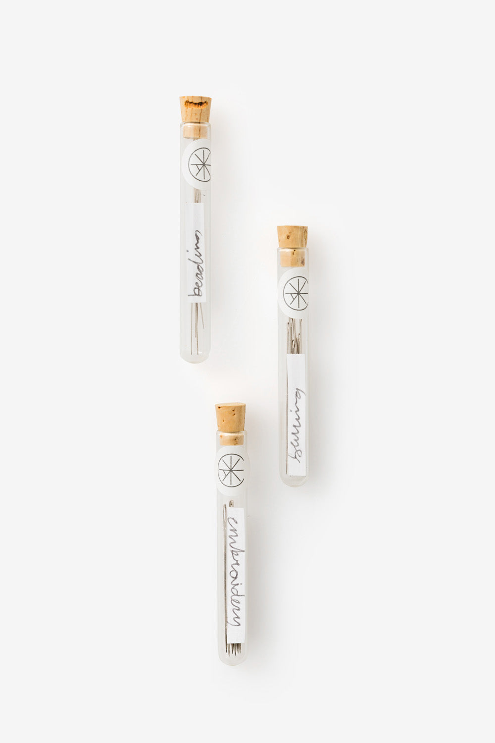 Three glass vials of needles: one each for beading, sewing, and embroidery.