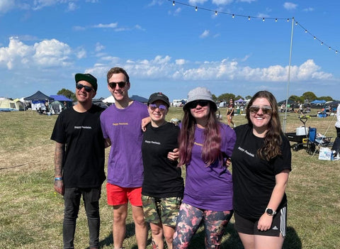 Friends wearing black and purple Happy Pessimist t-shirts smiling at the camera