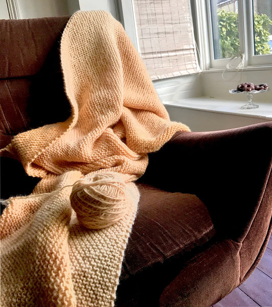 Hand knitted rose hip dyed woollen blanket on a G-Plan brown chair