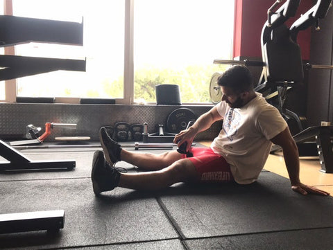 Hombre sobre una alfombra masajeando su cuádriceps con una pistola de masaje de terapia de percusión Topmet