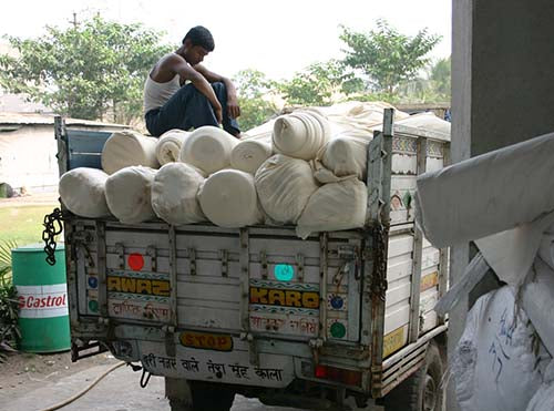 Arbeiter sitzt auf einem Stapel Stoffballen auf der Ladefläche eines LKW vor der Fabrik von Rajlakshmi Cotton Mills Pvt. Ltd. in Howrah, Kolkata, Indien