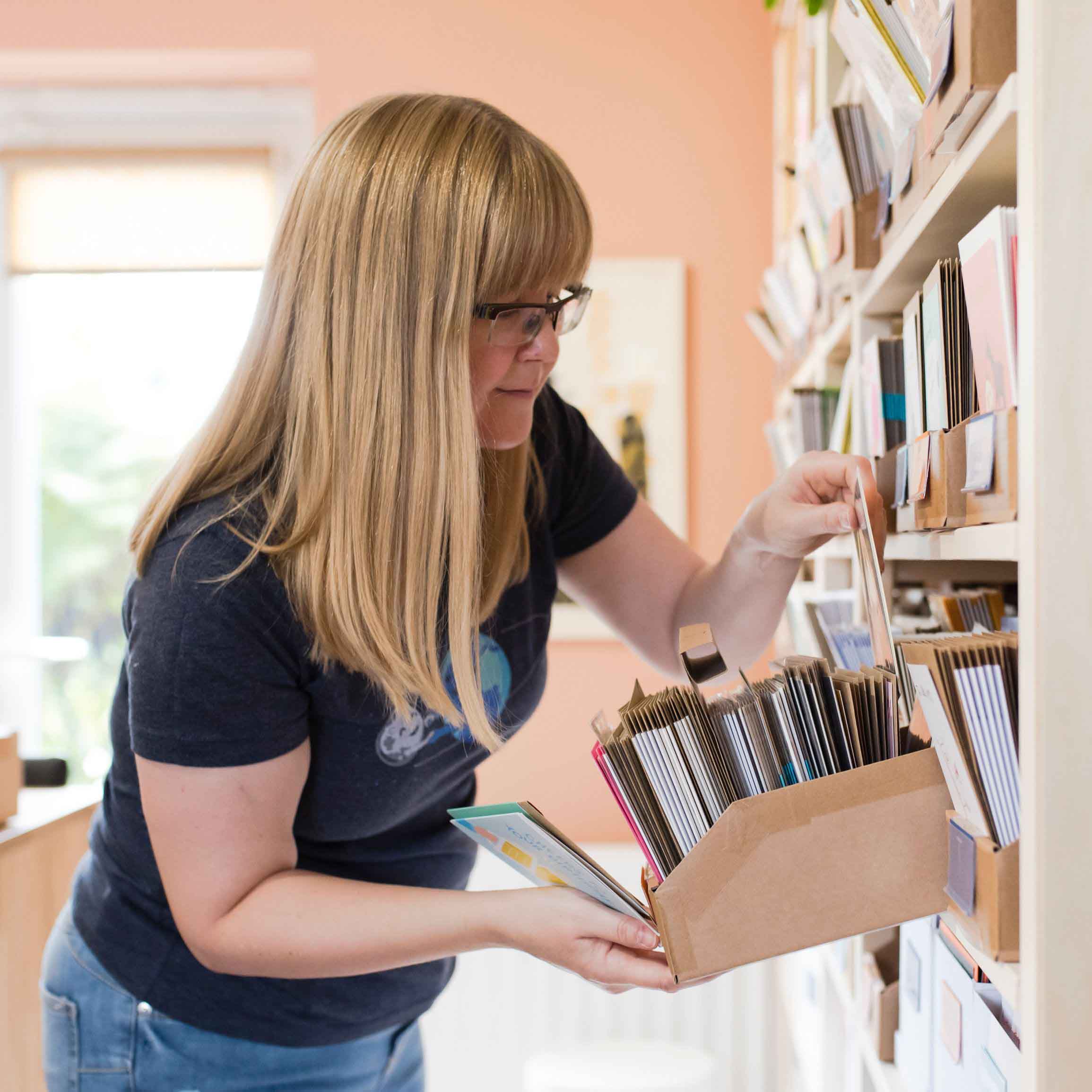 Claire picking an order from a shelf of brown boxes full of cards. Photo by Holly Booth