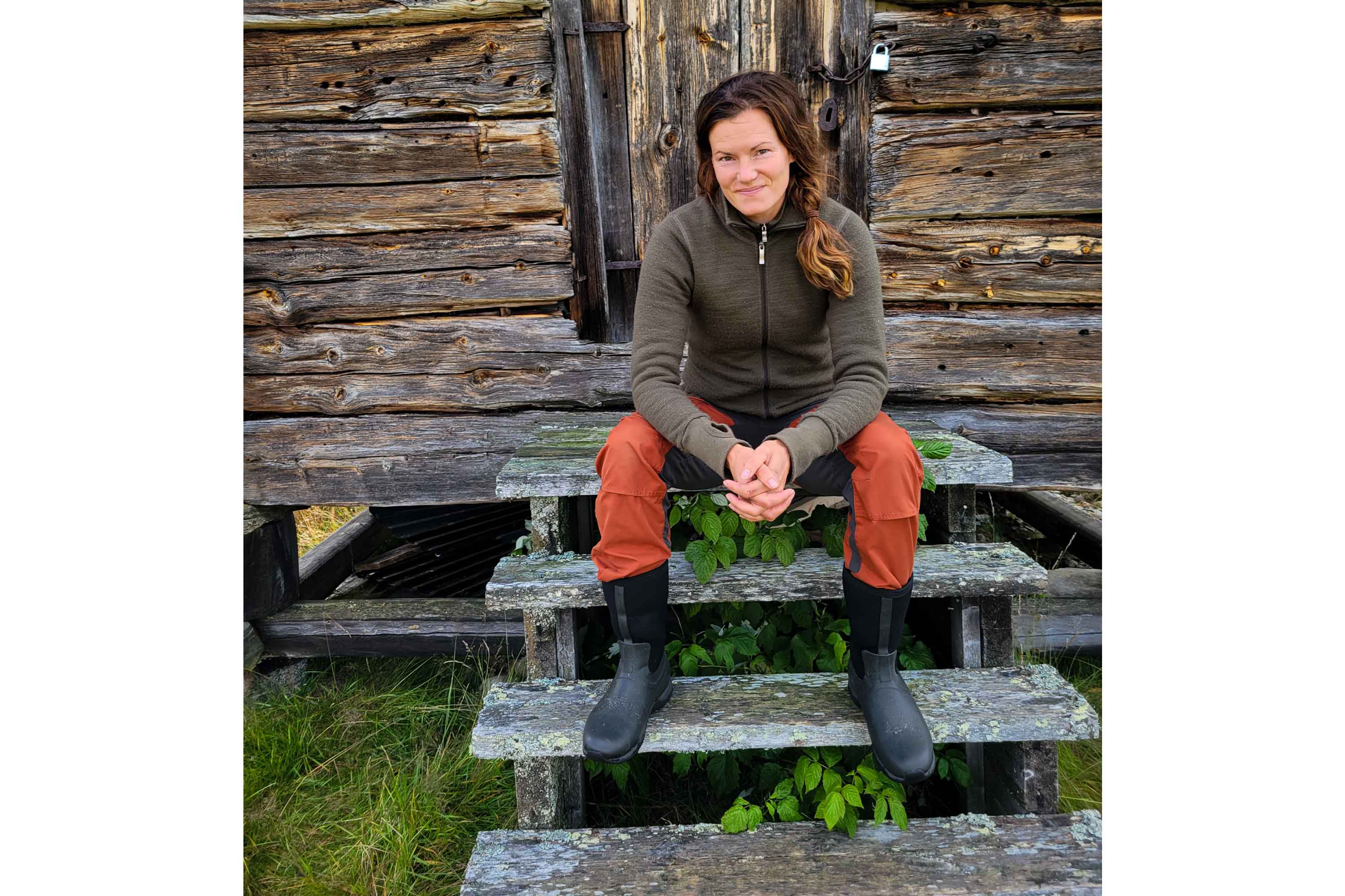 Nathalie Larsson sat on steps leading up to a wooden cabin, wearing a fleece, orange trousers and a pair of Muck Boots