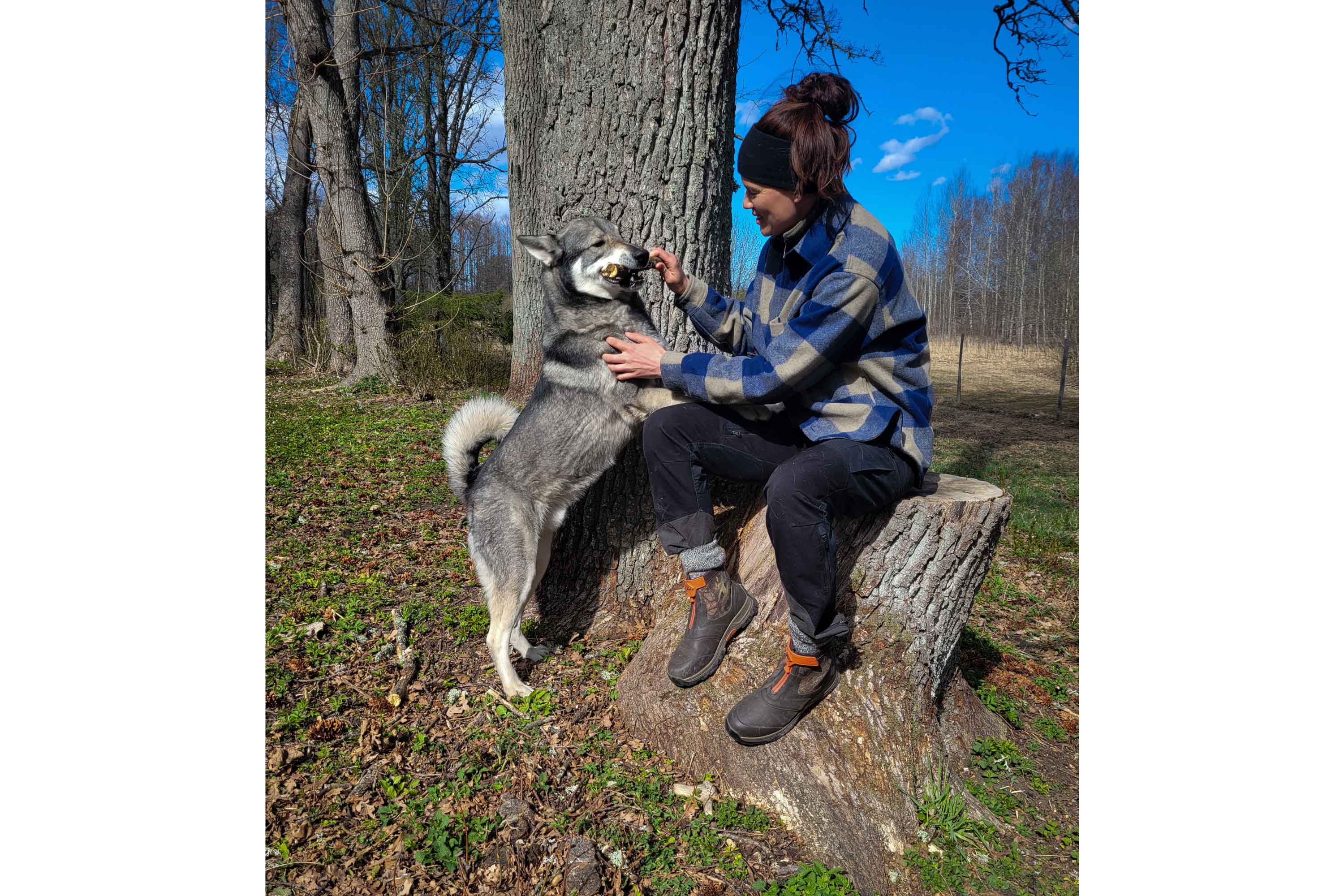 Nathalie Larsson sat on a tree stump, wearing cold weather clothing and a pair of Muck Boots. She's giving a bone to her dog