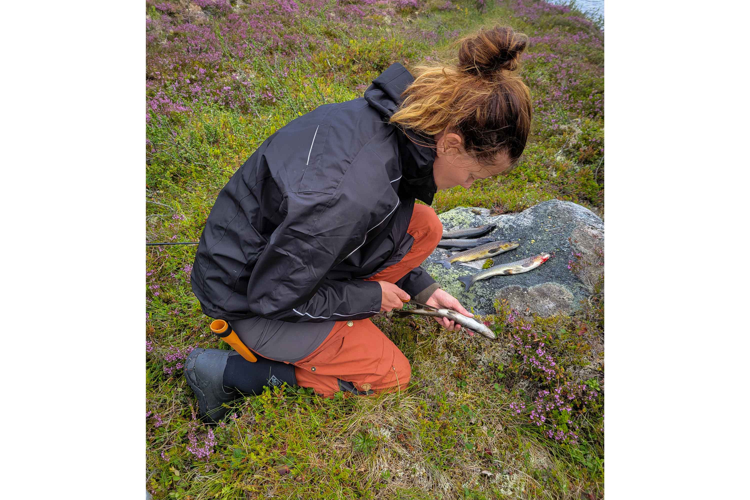 Nathalie Larsson wearing wet weather clothing and a pair of Muck Boots, cutting open freshly caught fish on a rock