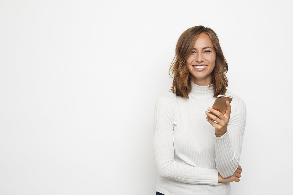 woman in white turtleneck holding iphone