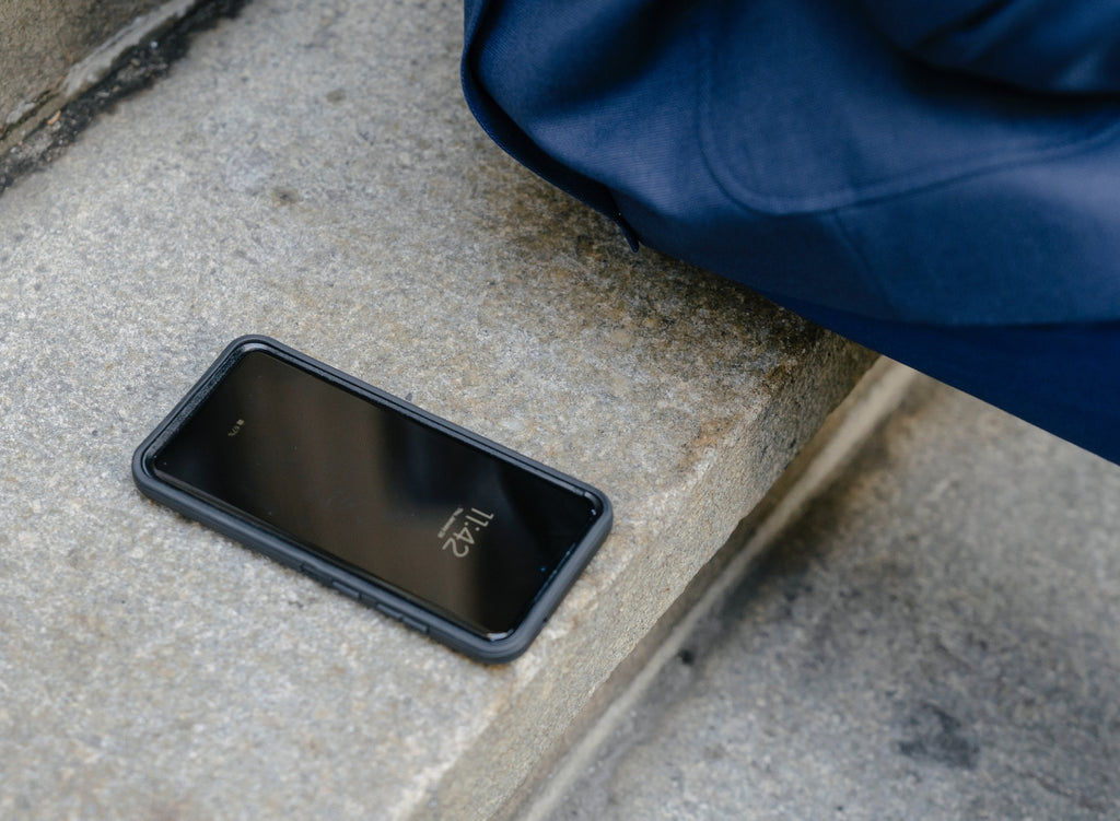 close up of smartphone sitting on the concrete beside someone sitting down on a stoop