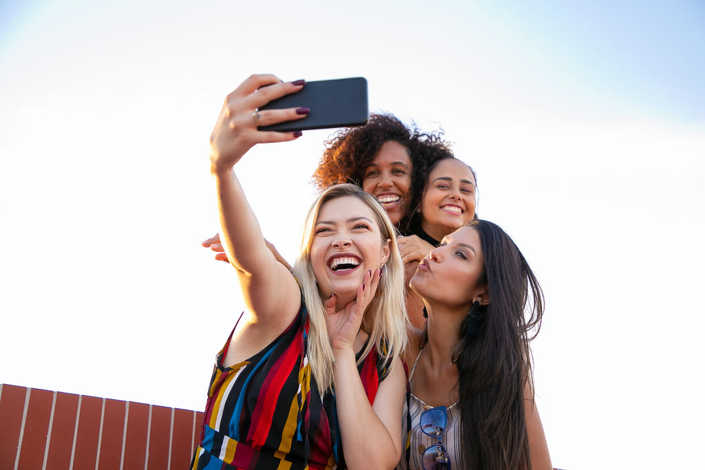 4 young women taking a group selfie outside