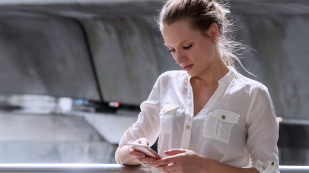woman staring down at iPhone in a white blouse