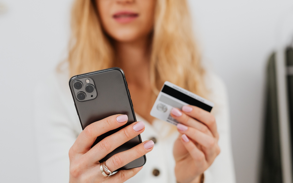Woman with a pink manicure holding an iPhone and credit card with a concerned face