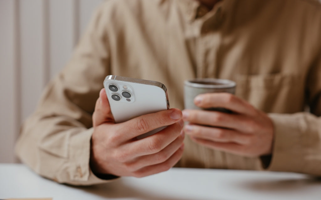 Man in camel colored shirt holding a cup of coffee and a white iPhone