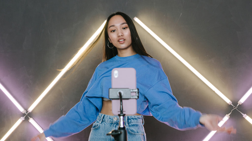 young woman in a blue cropped sweater making content in-front of an iPhone on a tripod