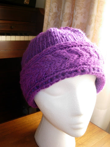 a styrofoam mannequin head wearing a purple cableknit hat, set on a piano bench by a window letting in diffused sunlight