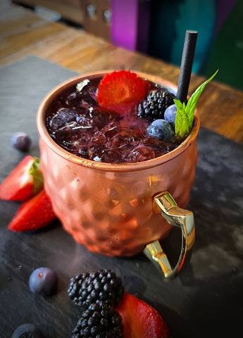 mixed berry moscow mule cocktail using mixed berry fruit infused vodka. Cocktail in copper moscow mule mug garnished with mixed berries and mint.