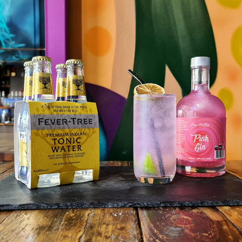 Fever Tree Indian Tonic Water four pack displayed with Newy Distillery Pink Shimmer Gin and Pink Shimmer Gin Gin and Tonic Drink in a tall glass with dried orange garnish. Newy Distillery Cocktails, gin and tonic.