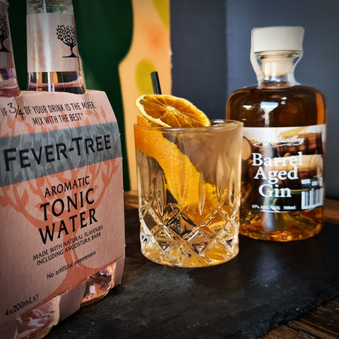 Fever Tree Aromatic Tonic Water four pack displayed with Newy Distillery barrel aged gin gin and tonic garnished with orange peel. Newy distillery cocktails with barrel aged gin.