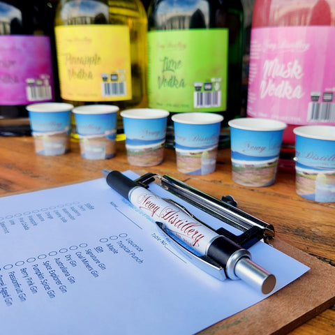 NEWY DISTILLERY FREE TASTING SESSION. Pen and clipboard infront of selection of flavoured vodkas. Musk vodka, Lime Vodka, Pineapple Vodka, Grape Vodka.