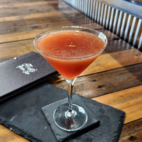 Newy Distillery Cocktail recipe. Missy's Maple Sour made with maple vodka. Orange cocktail in martini glass on grey slate. Wooden bar and cocktail menu.