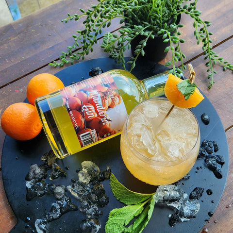 Mandarin Gin Collins Cocktail Recipe. Made with Newy Distillery Mandarin Gin. Mandarin Gin Collins cocktail with mandarin orange and mint garnish on a black chopping board, surrounded by ice, mandarin oranges and mint sprig. Placed next to a bottle of Newy Distillert Mandarin Gin.