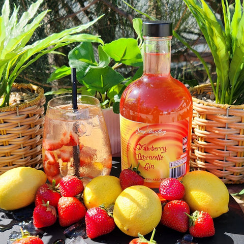 Newy Distillery Strawberry Limoncello Liqueur. GinLimoncello infused with fresh strawberries. 500ml bottle displayed next to Strawberry Limoncello Gin cocktail, surrounded by lemons and strawberries. Green plants in the background.