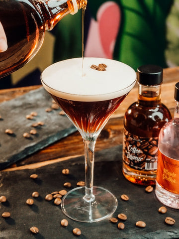 Maple Syrup Espresso Martini Cocktail Recipe. Cocktail in martini glass with maple syrup being poured into it. Served on grey slate with coffee beans scattered around. Maple Syrup Vodka. Cocktail recipe by Newy Distillery.