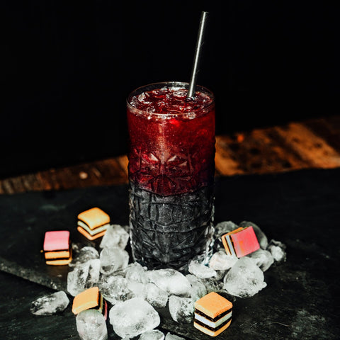 Liquourice and Raspberry cocktail by Newy Distillery. Displayed with ice and liquorice all-sorts on grey slate. 