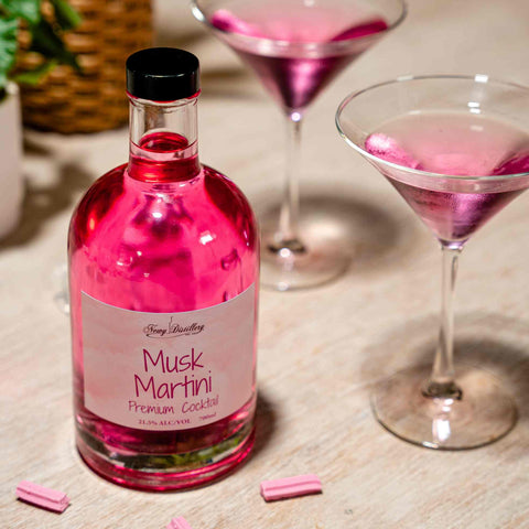 Newy Distillery Musk Martini Pre-MIx Cocktail Bottle 700ml. Ready to serve musk vodka cocktail drink displayed on white table with scattering of musk sticks and two pink cocktails served in martini glasses.