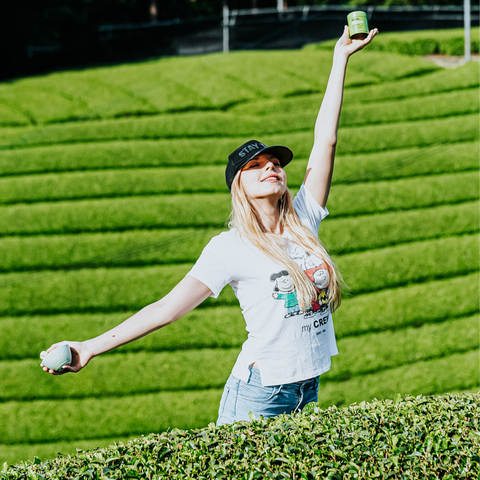 Woman with open arms holding matcha in the green fields of Japan 