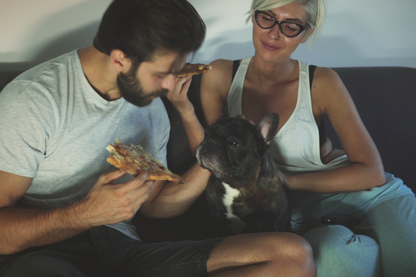 couple eating pizza with their dog in the middle