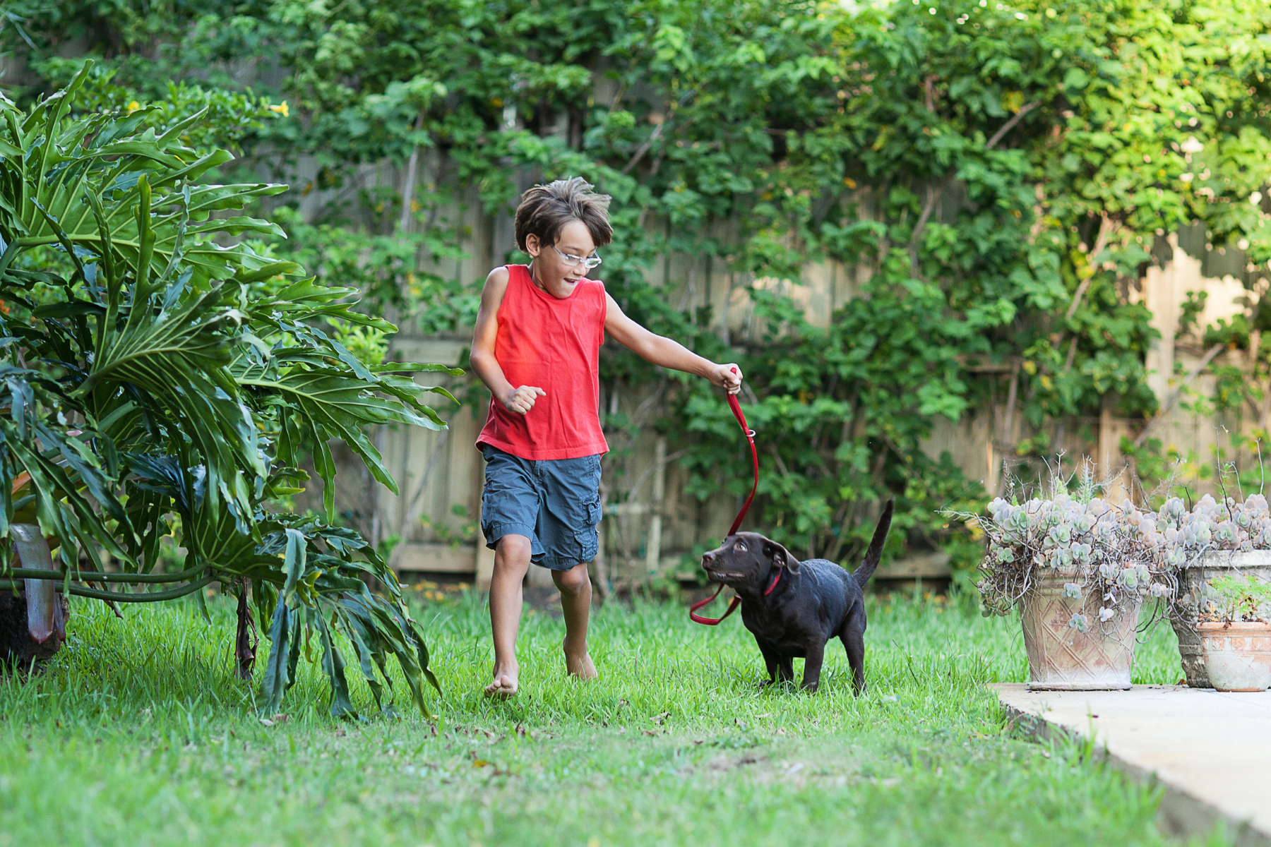 boy in red shirt running on the grass with a black dog