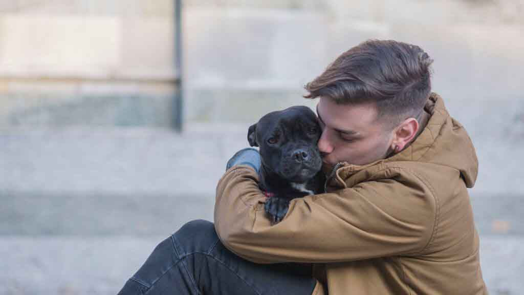 man in tan jacket snuggling with black pug