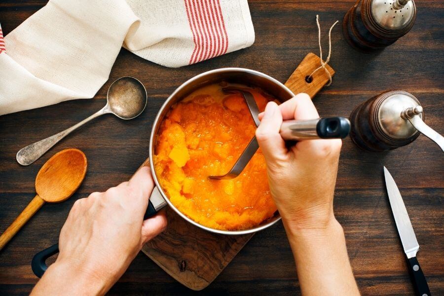 person mashing pumpkin into puree in a pot