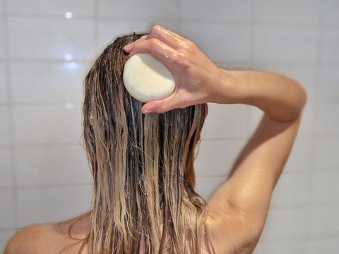 Girl with blonde wet hair is using a white coloured Hair Cooki shampoo bar