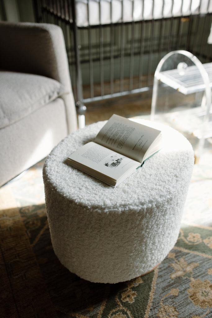 Sheepskin Cloud ottoman with book on it and acrylic stool behind.