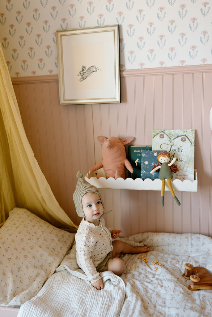 toddler sitting on bed with scallop shelf