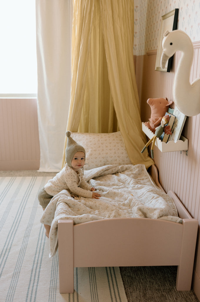 baby leaning on toddler bed with floral bedding