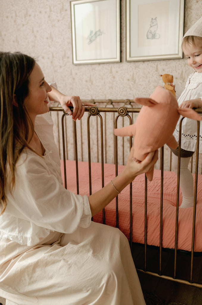 oilo rosette crib sheet with toddler in crib and mother handing him a toy