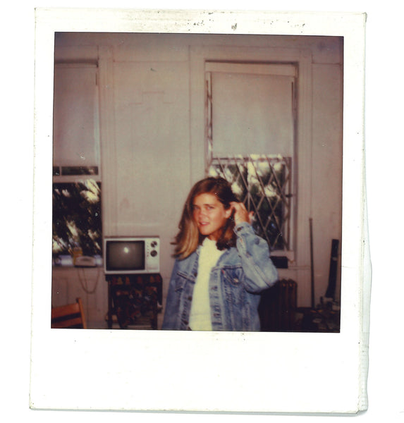 Ann in her very first apartment in Nolita. She's wearing a denim jacket and standing in front of two windows. There's a little TV in the background — she notes there wasn't room for a whole lot else.