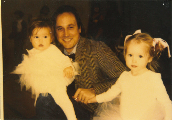 Sid holding Elizabeth and Louisa at their ballet recital. They're wearing pink ballet skirts and have ribbons in their hair.