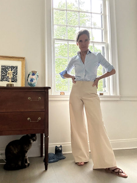 Ann at home in a sky poplin button down, strappy sandals, and the Fallon Pull-On Pants in Sand.