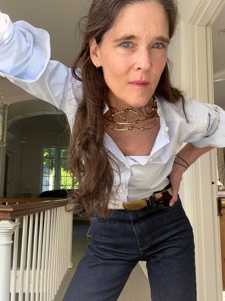 Ann at home in a sky poplin button down, denim with a zebra belt, and a gold collar necklace made by Gogo. 